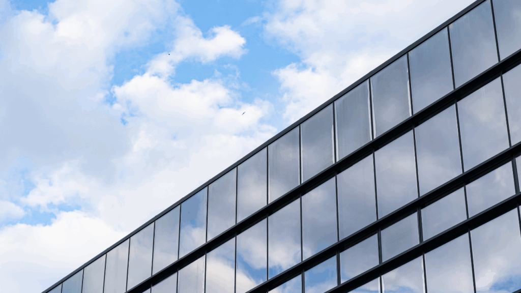 Fachada de prédio comercial com painéis de vidro refletindo o céu azul e nuvens.