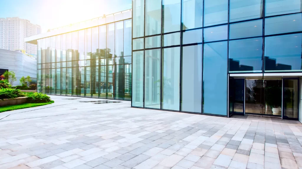 Entrada de edifício moderno com fachada de vidro refletindo a cidade ao redor.