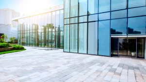 Entrada de edifício moderno com fachada de vidro refletindo a cidade ao redor.